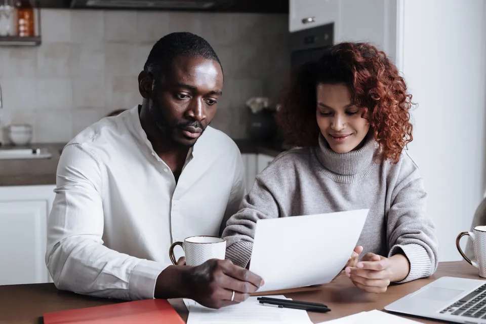 A couple reviews paperwork at a kitchen table, embodying teamwork and collaboration.