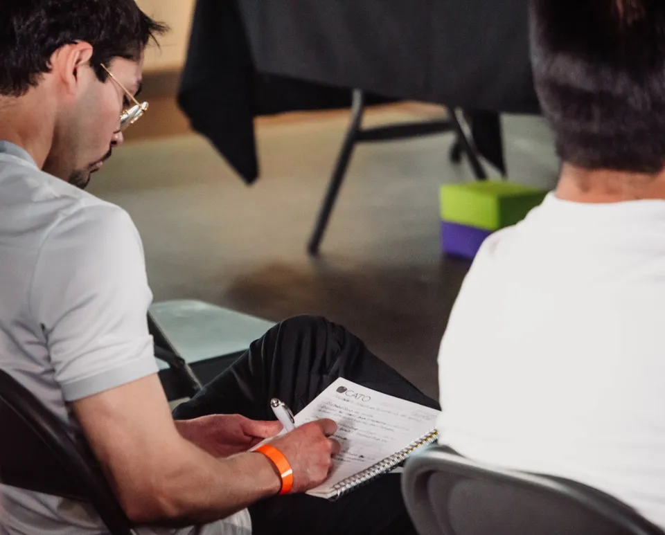 A man attentively taking notes during an indoor seminar, focused on learning.