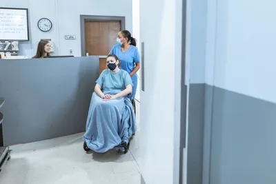 Nurse assisting a patient in a wheelchair at a medical facility reception.