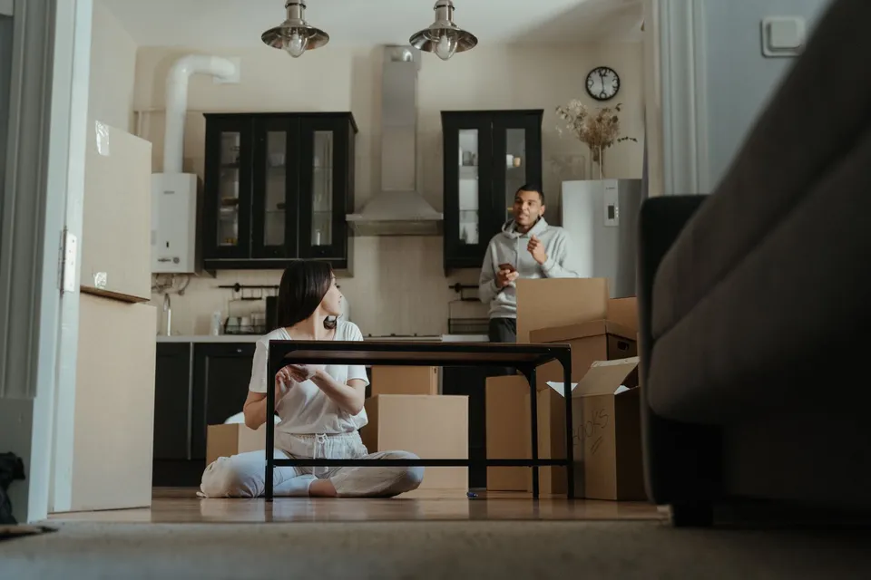 A couple is seen unpacking boxes in their new apartment, setting up their kitchen area.