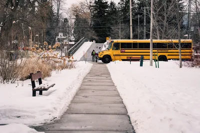 A school bus parked near a snowy sidewalk during winter, with people walking nearby.